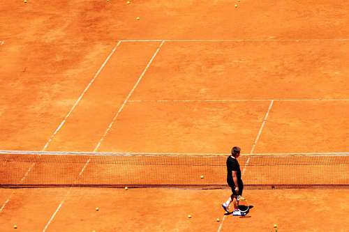 A man walking in a tennis red yellow ball on a clay tennis court orange color