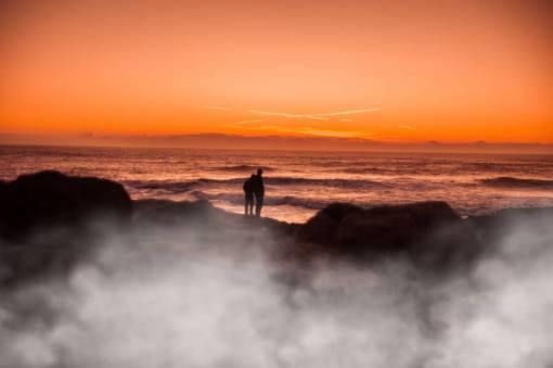 apuntalar océano puesta de sol pareja personas silueta rocas orilla
