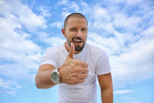 arriba hombre pulgares arriba guiño sonrisa feliz cielo azul nubes