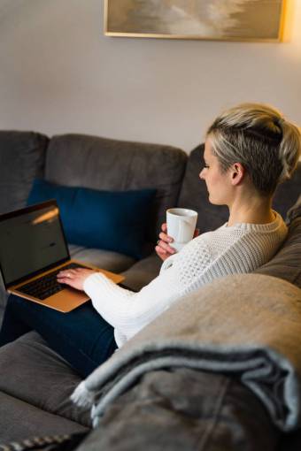morning Woman having a coffee while working with her laptop in the armchair