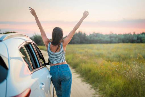landscape Woman in the field on her back with her arms raised next to her car