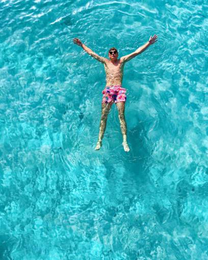 Young man floating with open arms over turquoise water 