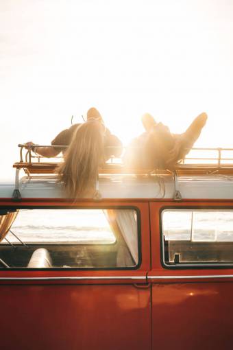enjoyment Two young women relaxing on the roof of a van at sunset by the sea