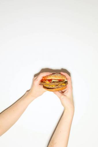 tenencia Mano sujetando una hamburguesa con queso sobre fondo blanco.