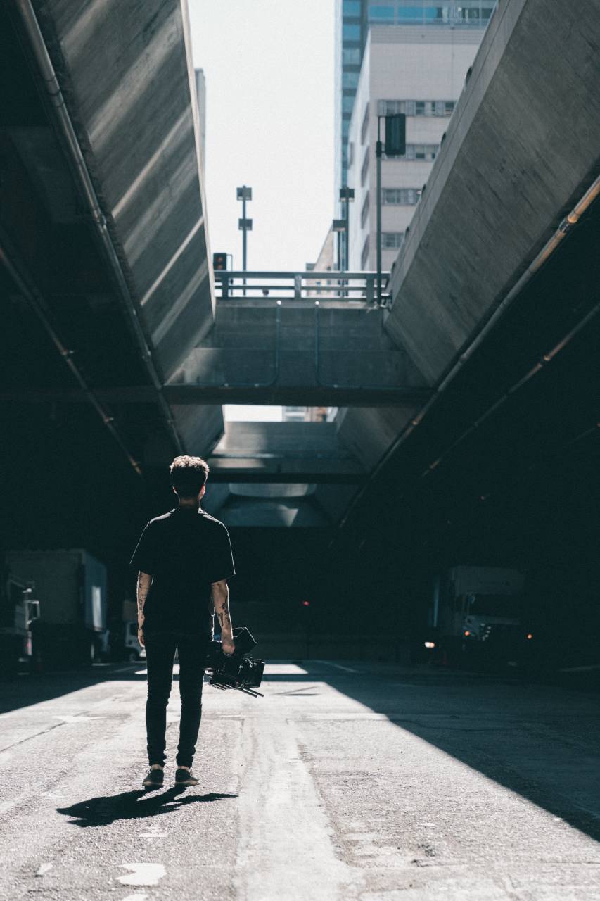 people, man, shadow, guy, day, bridge, fence, stoplight, back, sky way, high way, vehicles, camera, video, recording, filming, photographer, road, building, sky
, 