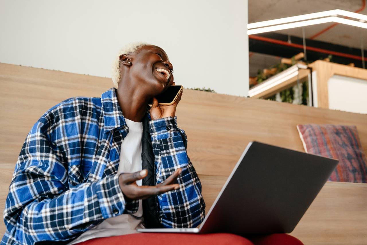 mujer;afroamericano;sonriendo;computadora;hablando,hombres,tecnología,una persona,varones,adulto,tecnología inalámbrica,trabajo,adulto joven,teléfono móvil,estilos de vida,sentado,interior,etnia africana,comunicación,internet,ropa casual,sonriendo, Laptop,computadora,teléfono,teléfono inteligente,hablando,uno,hombre,buscando,e-mail,felicidad,empresario,relajación,conexión,alegre,discusión,