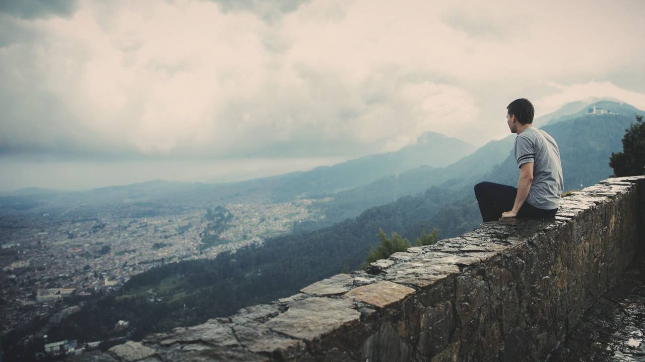 Guy, mirando, sentado, cornisa, ciudad, pueblo, montañas, valles, colinas, nubes, ver gente,