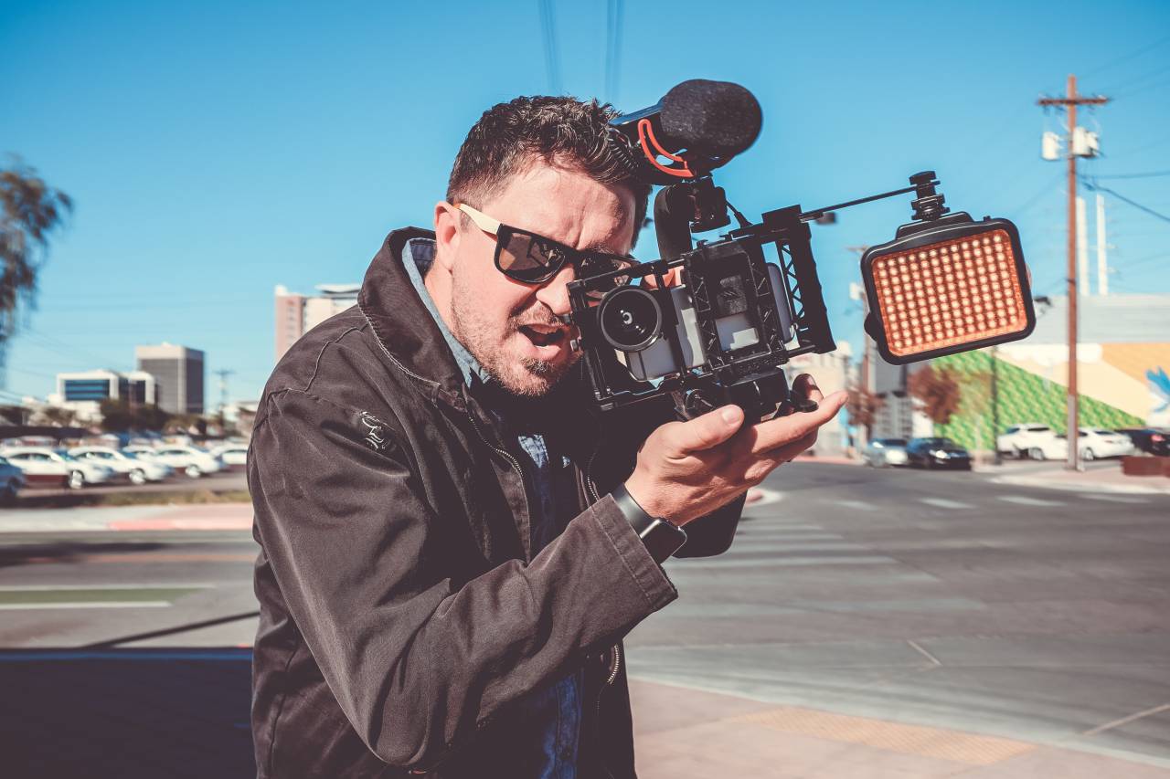 camarógrafo, hombre, chico, micrófono, carretera, calle, luz, lente, macho, luz del sol, coches, edificio, puesto, chaqueta, negro, película,