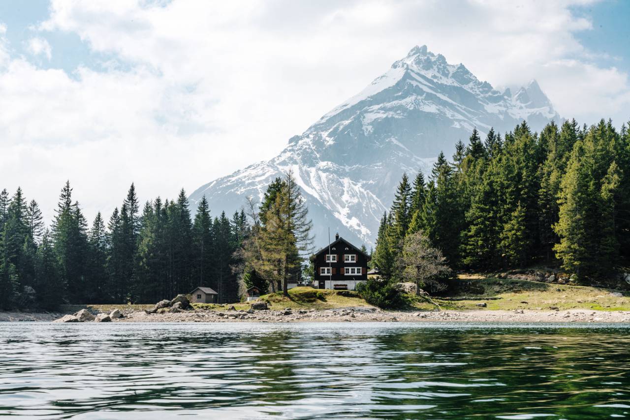 naturaleza, paisaje, montañas, cumbre, picos, nieve, bosque, árboles, apuntalar, arena, rocas, césped, agua, lago, ondas, superficie, casa, cabaña, cabaña, nubes del cielo,