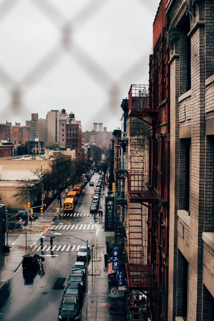 people, man, woman, vehicle, car, bus, lane, line, pedestrian, crossing, stoplight, street, urban, building, infrastructure, architecture, establishment, trees, fence, rooftop
, 