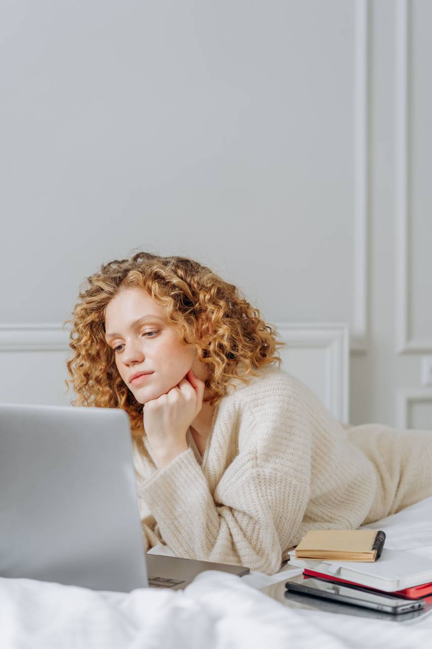 cara,adentro,una persona,computadora portátil,etnicidad caucásica,tecnología,estilos de vida,interior de la casa,mujer,computadora,cabello rizado,adulto,relajación,mujeres,tecnología inalámbrica,trabajando,internet,niño,adulto joven,sentado,sonriendo,dormitorio, ropa casual, educación, estudio, infancia,