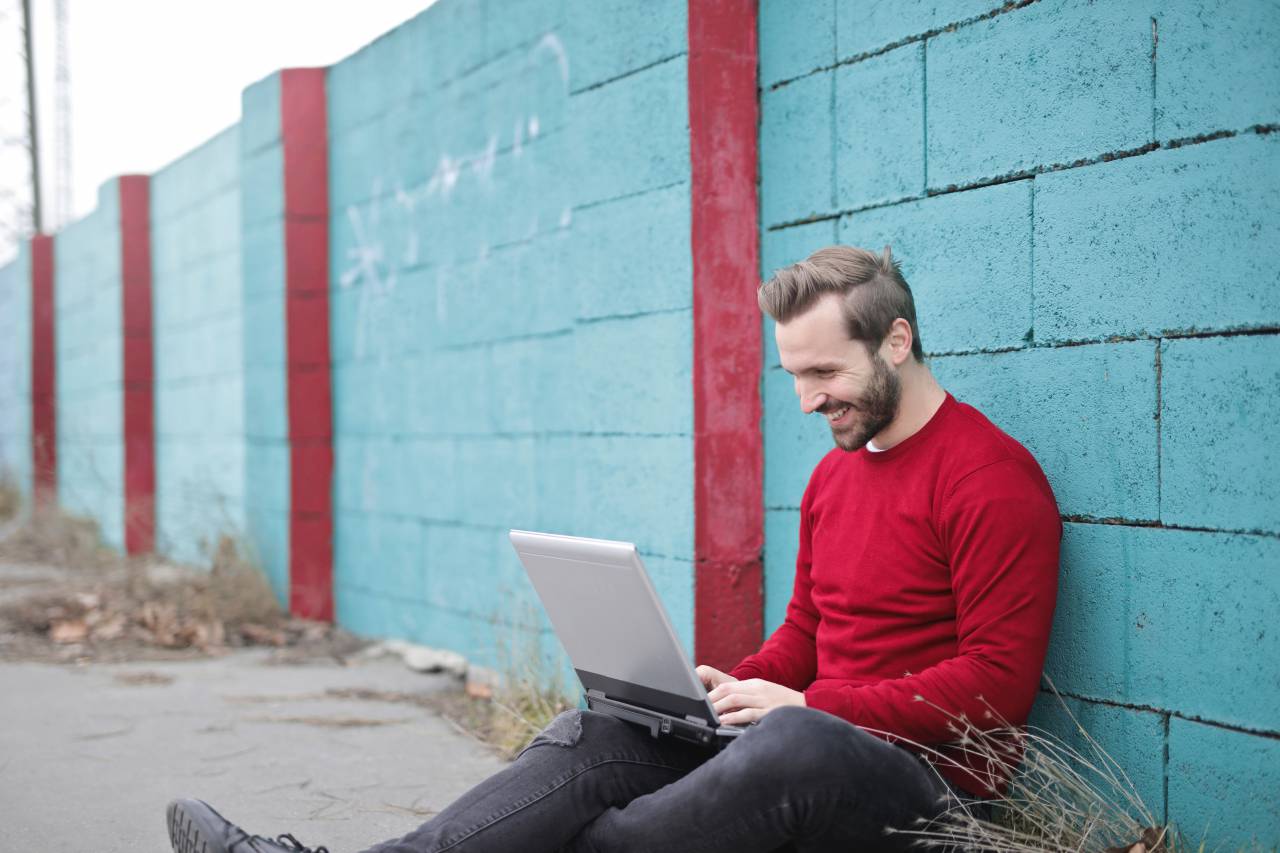 man, laptop, smile, happy, technology, computer, brick, wall, blue, fashion, red, jumper, jersey, jeans
, 