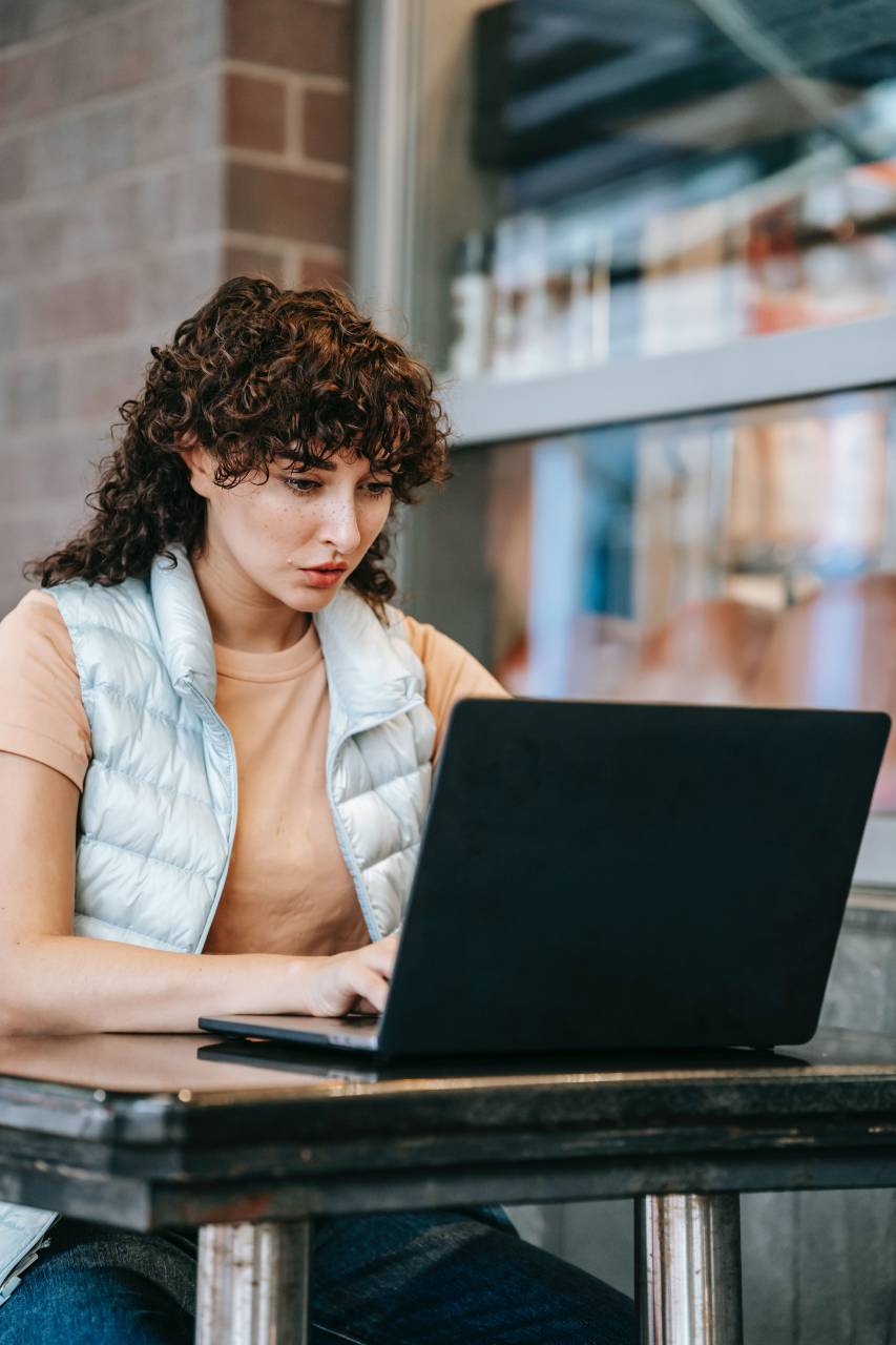 Woman, Laptop, Working, Cafe, Productivity, Focused, RemoteWork, Coffee, Casual, Technology, Professional, Relaxed, Busy, Modern, Business, jacket vest, curly, 