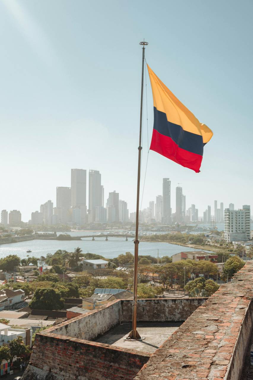 Colombian flag, Cartagena skyline, Colombia flag waving, cityscape, Caribbean city, historic Cartagena, flag and city, patriotic symbol, coastal city, urban panorama, South America, city skyline, national pride, colorful flag, Caribbean coast, travel Colombia, tropical city, city view, historic architecture, flag in wind, waterfront city, travel destination, Colombian culture, city background, vibrant cityscape, flag close-up, coastal skyline, Caribbean architecture, city horizon, travel photography, city and flag, latinamerican, 