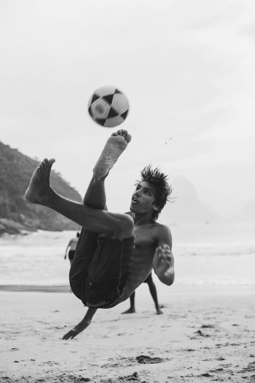 man playing football, Rio de Janeiro soccer, street football, Brazilian football, soccer player, urban sports, football action, Rio de Janeiro city, beach soccer, street athlete, soccer game, Brazilian culture, outdoor sports, football passion, athletic movement, sport in Brazil, casual football, football player kicking, Rio sports, soccer skills, street play, athletic man, football training, sports lifestyle, Brazil cityscape, football enthusiast, dynamic movement, soccer ball, outdoor activity, sports culture, latinamerican, 