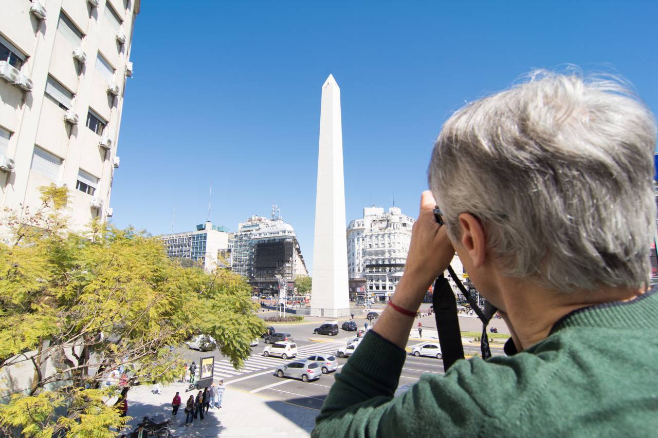 9 de Julio Avenue, Obelisk, Buenos Aires, Argentina, Landmark, Iconic, Traffic, Cityscape, Urban, Downtown, Skyline, Architecture, History, Monument, Tourist Attraction, Travel Destination, South America, Latin America, Stock Image, Street, Intersection, Cars, Buses, Pedestrians, one person, man, photographer, camera, shot, 
