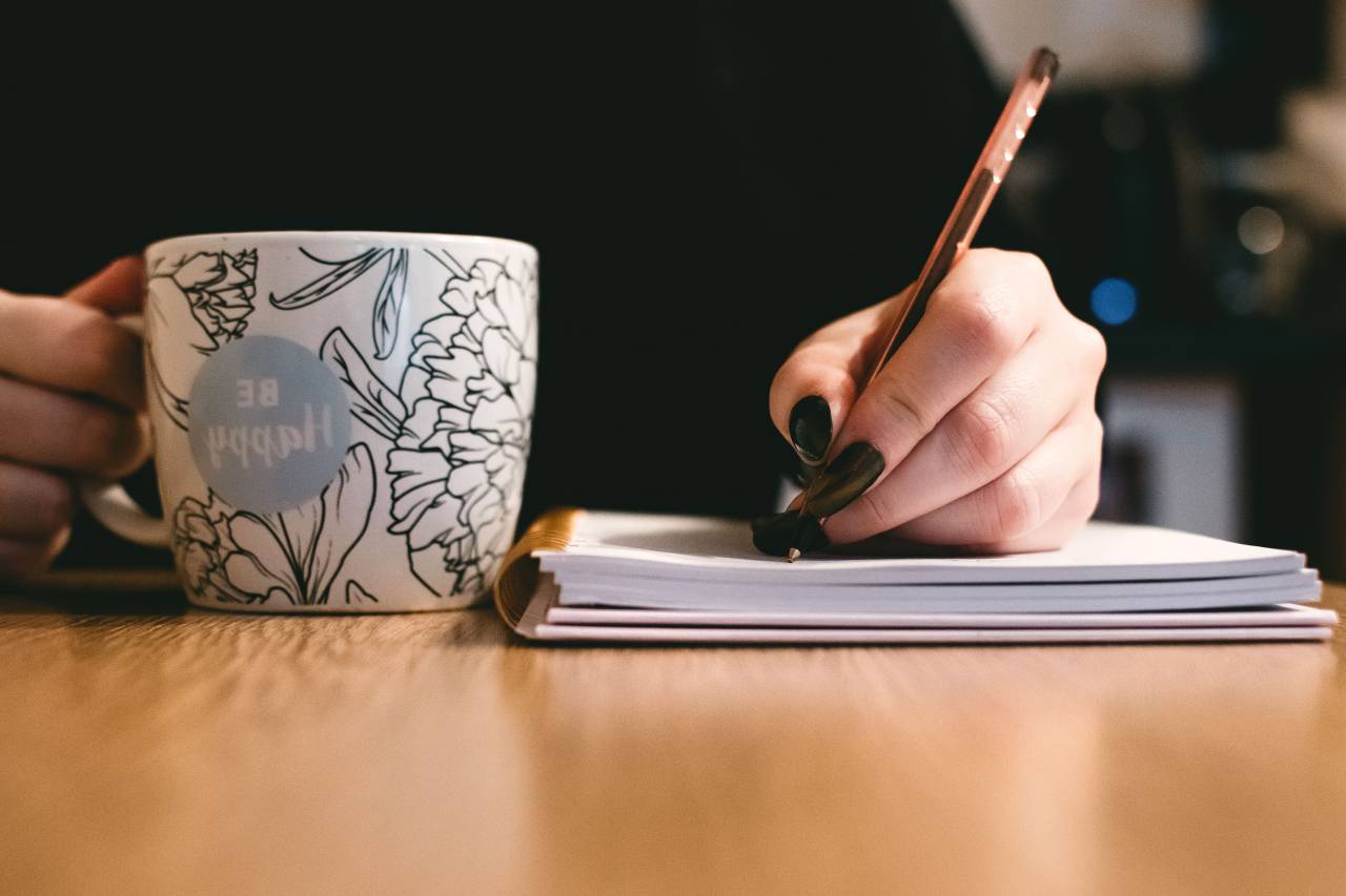 Ser feliz, taza, café, mujer, tenencia, bolígrafo, bloc de notas, escritura, cuaderno, madera, escritorio, oficina, negocios, patrón,