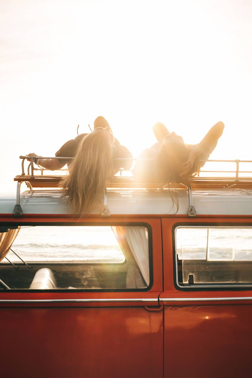 Two Young Women, Relaxing, Roof of Van, Sunset, Sea, Leisure, Friends, Bonding, Adventure, Coastal, Horizon, Tranquility, Golden Hour, Serene, Beach, Travel, Freedom, Outdoor, Enjoyment, Unwind, 